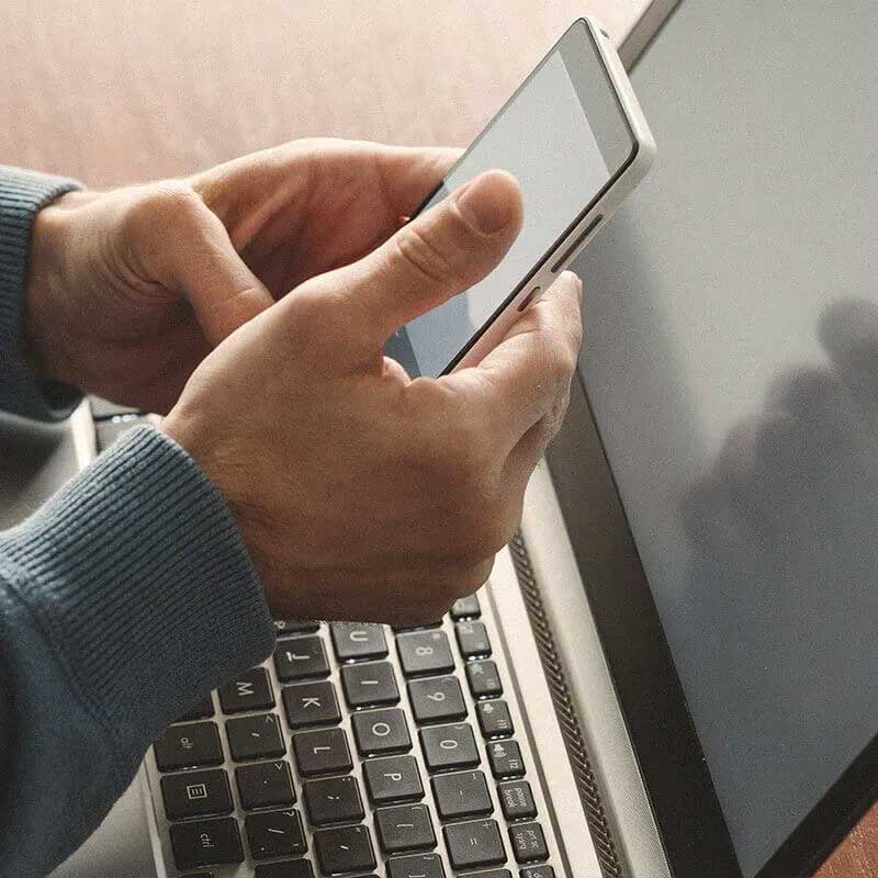 mains tenant un téléphone portable avec un ordinateur portable en arrière-plan