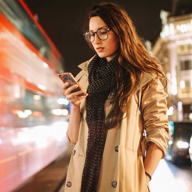 woman wearing glasses and a coat looking down at phone held in right hand